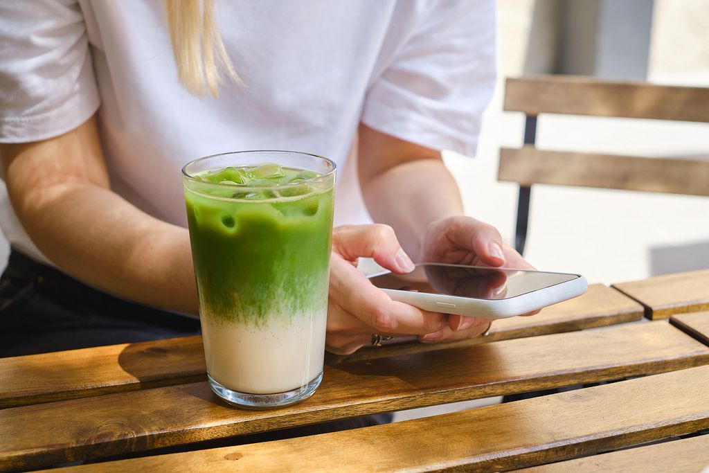 Person bedient ein Handy, neben sich einen Matcha-Tee.